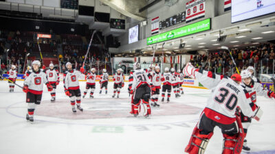 67's players celebrating on the ice after the game raising their sticks to the crowd